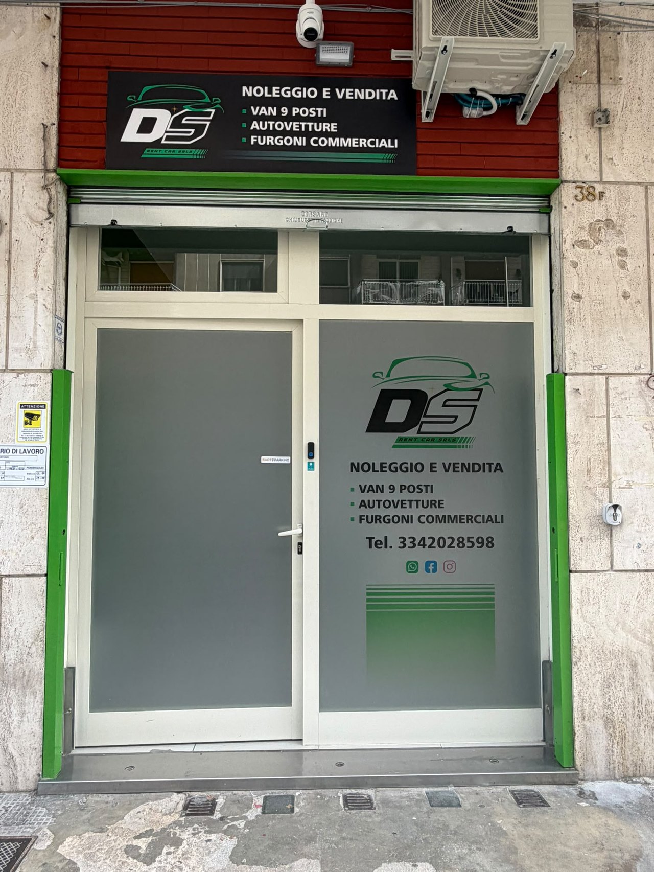 Ingresso di DS Rentcar con porta vetrata grigia, cornice verde e insegna «Noleggio e vendita, van 9 posti, furgoni commerciali