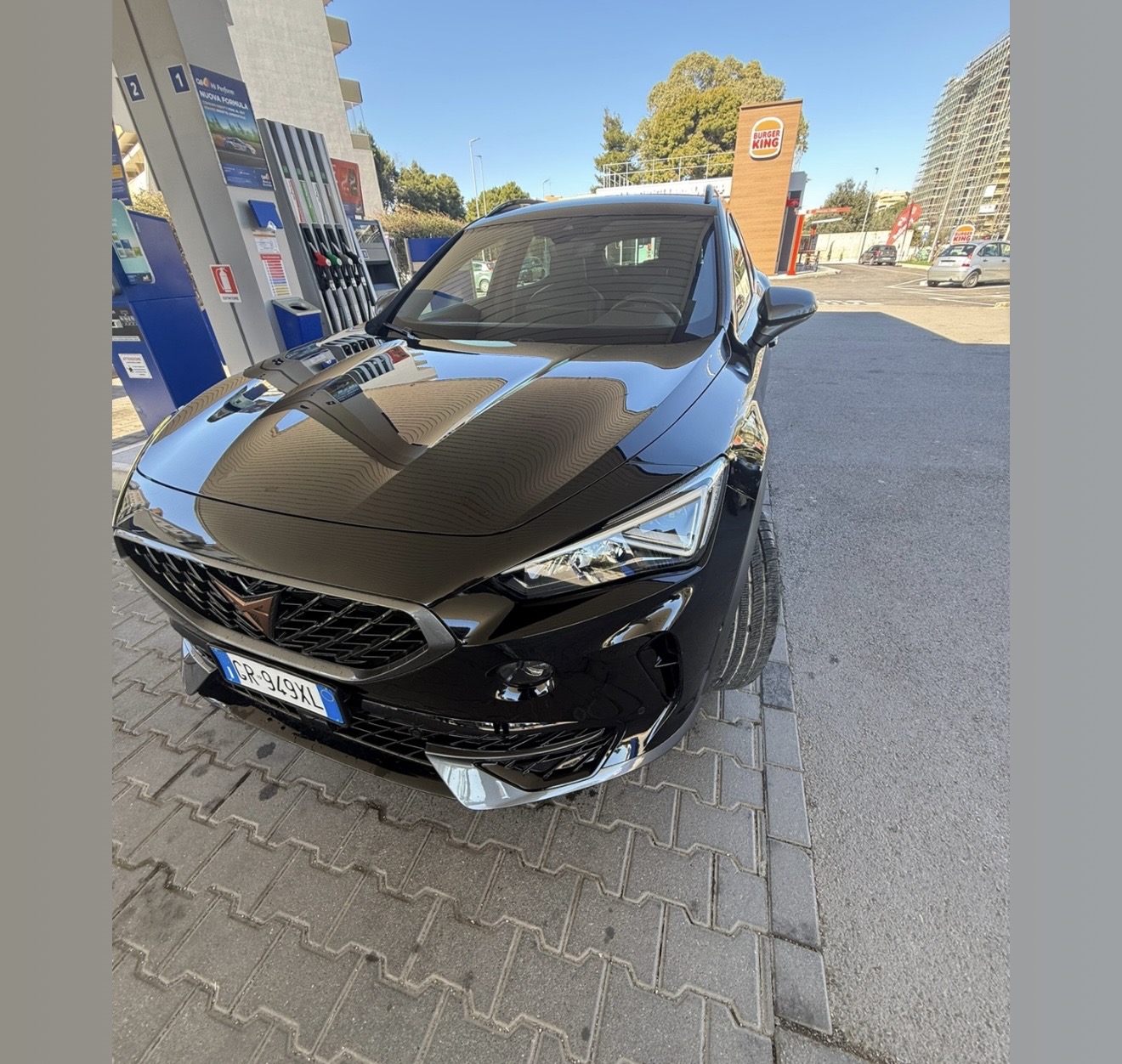 SUV Cupra nero con logo ramato fermo accanto alle pompe di un distributore, insegna Burger King sullo sfondo